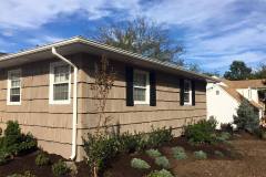 Professional painters in Suffolk County New York stain an exterior of a home tan with black shutters and white trim