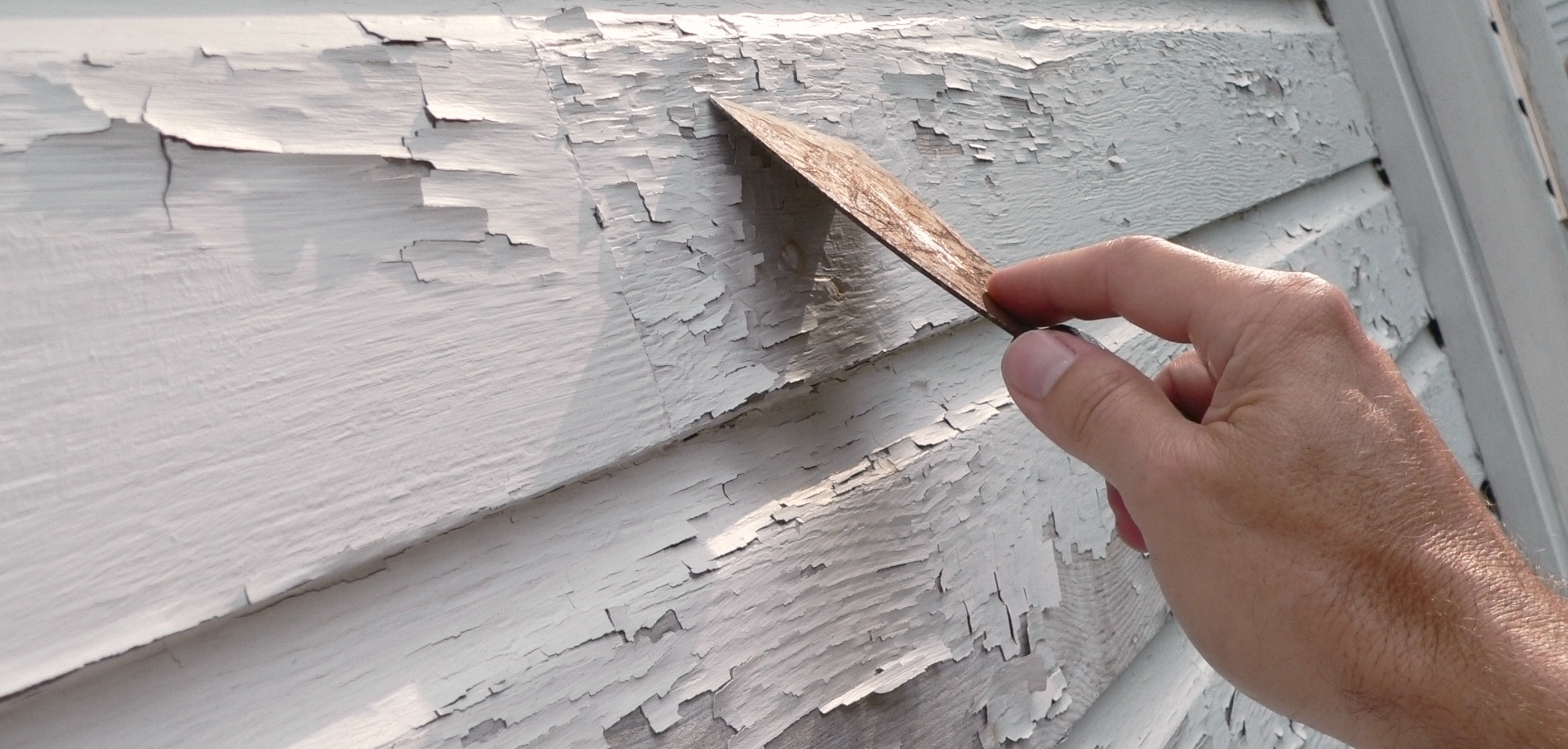 Professional house painter scraping peeling exterior paint on a Suffolk County NY home.